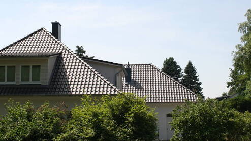 Dachsanierung Blick auf ein großes Haus mit schwarzen Dachziegeln